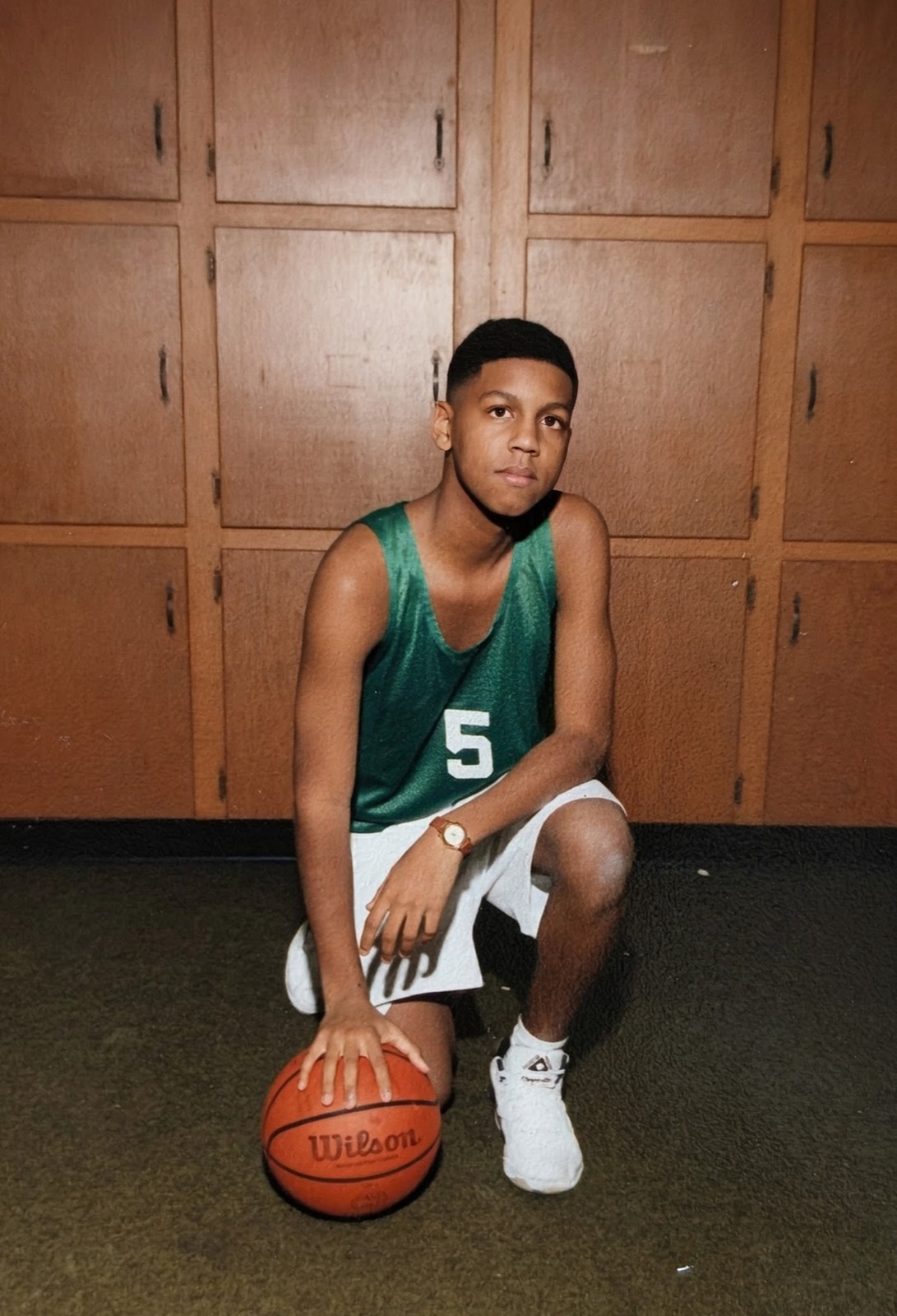 Kenny as a young boy kneeling with a basketball in his team uniform